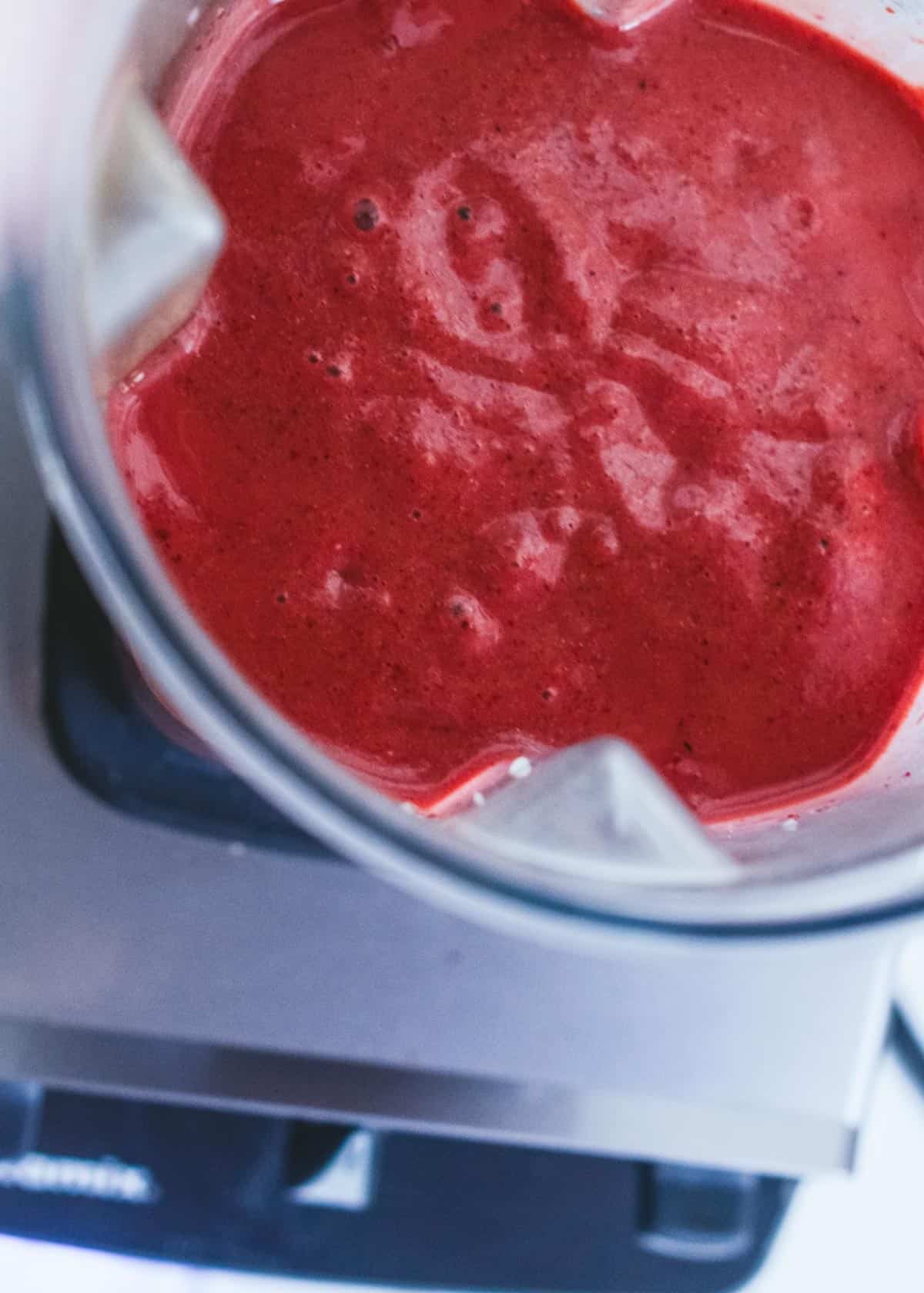 Dark red smoothie in a vitamin container, sitting on the vitamix.