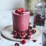Dark red smoothie with frozen cherries and raspberries sitting on it with a jar of hemp hearts behind it.