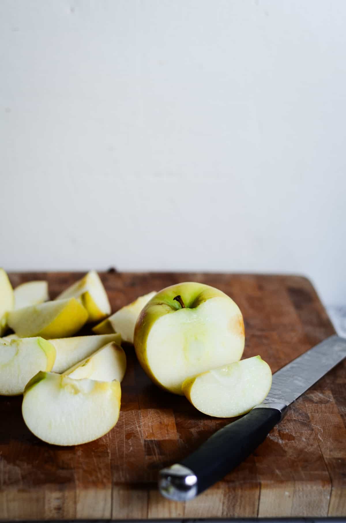 Apples being chopped on a wooden cutting board to freeze for a smoothie.