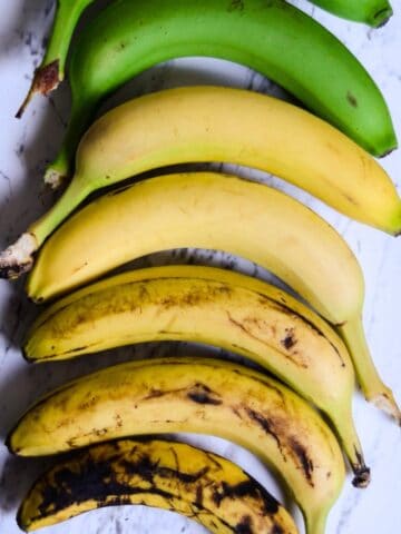 Green bananas, yellow bananas, and brown bananas laying on the counter.
