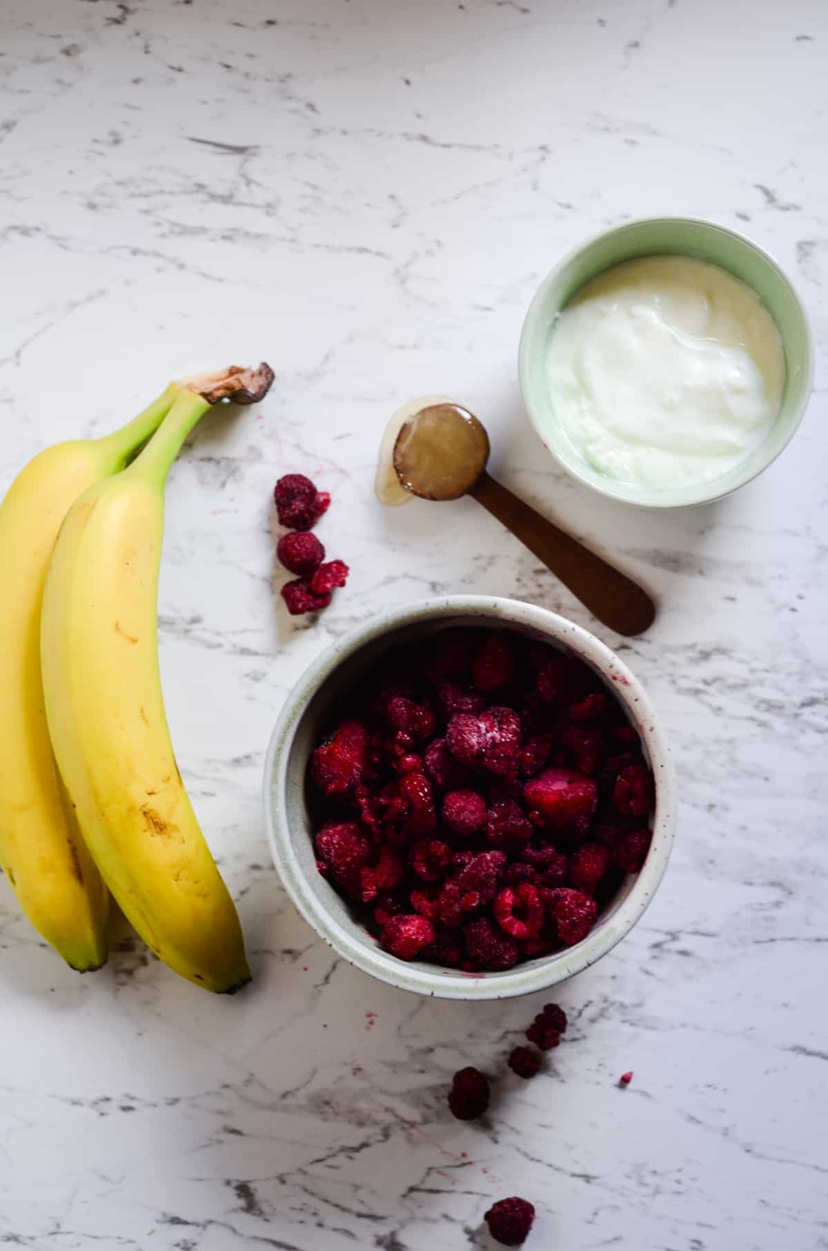 Bananas, frozen raspberries, yogurt, and honey on the counter for a smoothie.