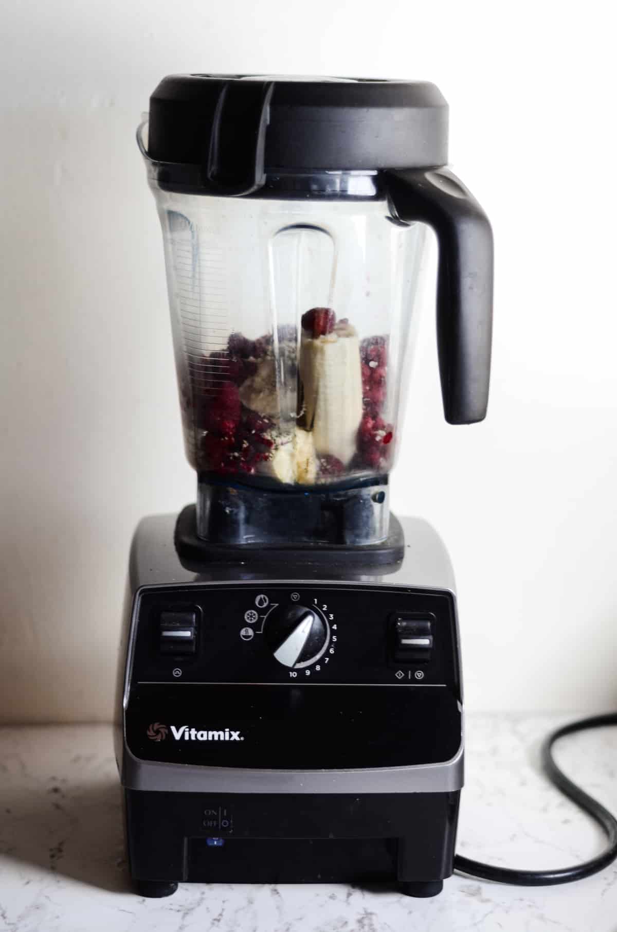 Vitamix container on the machine stand read to blend a raspberry smoothie.