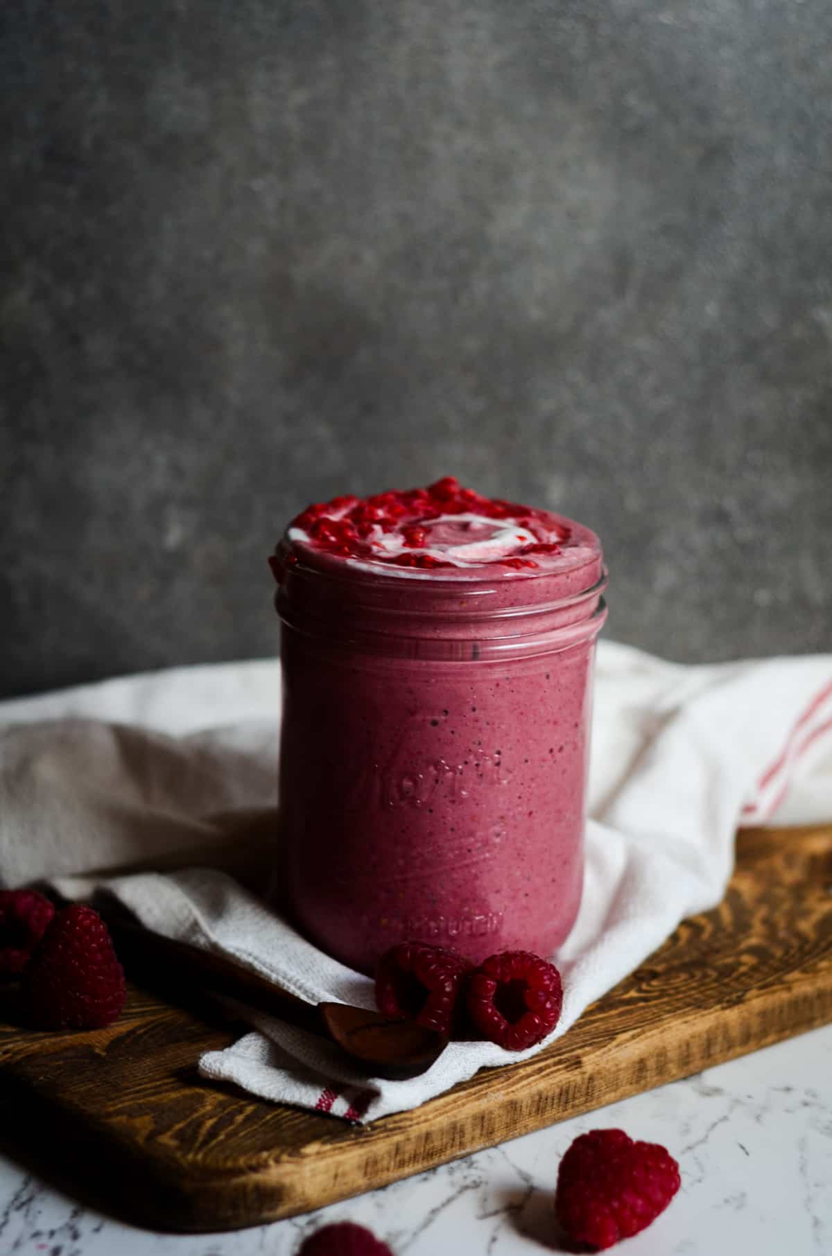 Raspberry smoothie in a jar with yogurt swirled on top sitting on the counter.