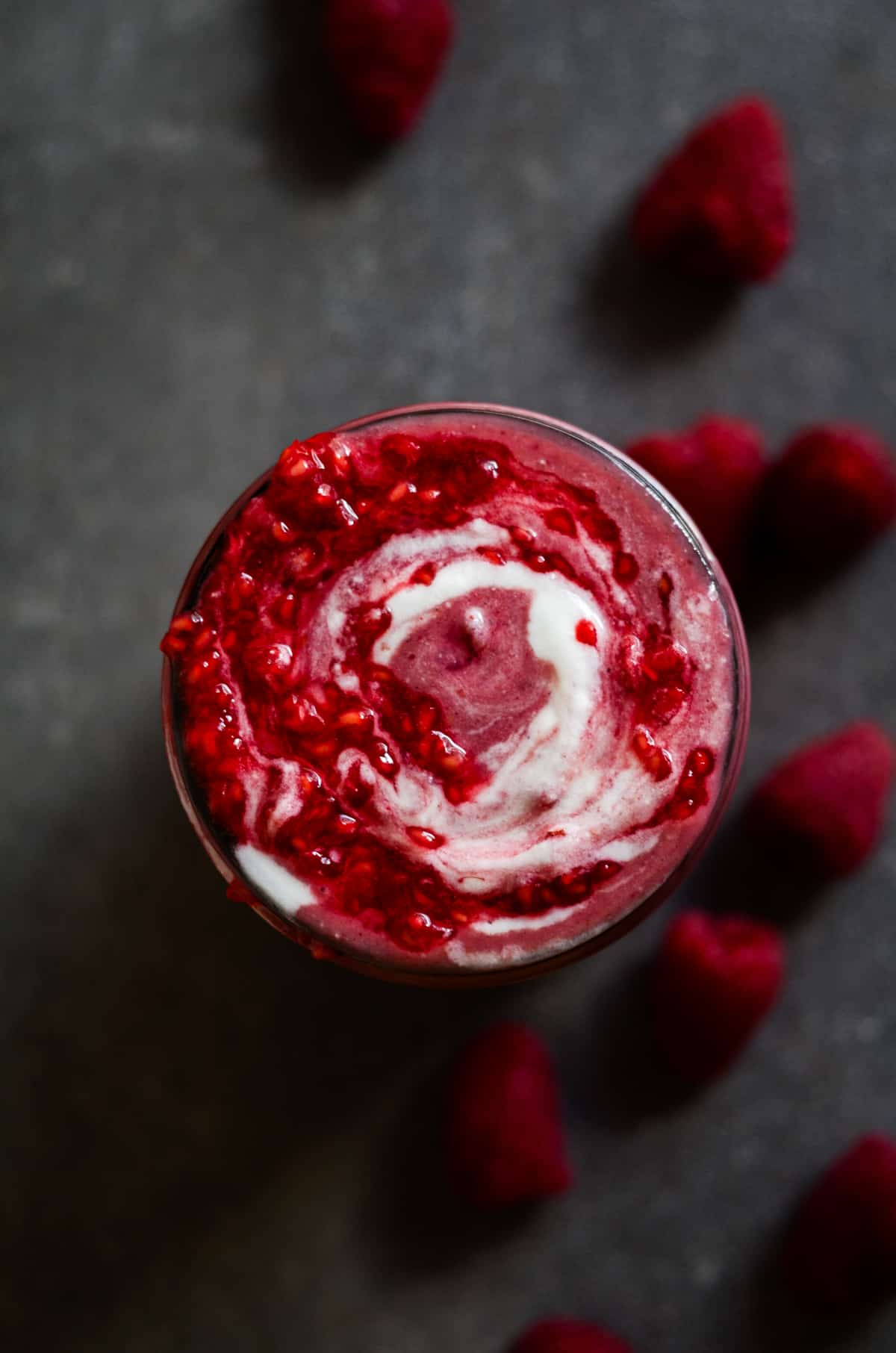 A beautiful pink raspberry smoothie with yogurt and fresh smashed raspberry on top.