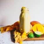 Light yellow smoothie in a glass jar for drinking with a fresh mango and lime on the counter.