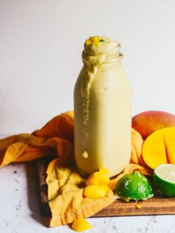 Light yellow smoothie in a glass jar for drinking with a fresh mango and lime on the counter.