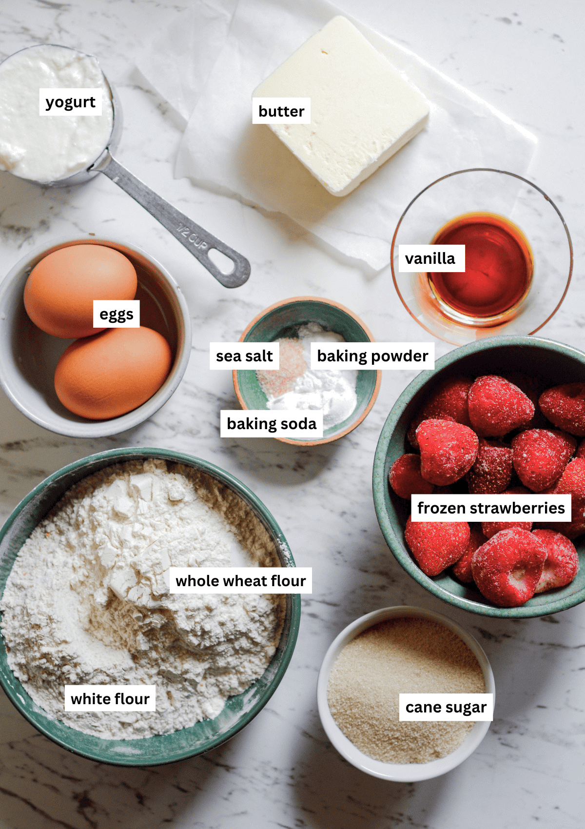 Ingredients for muffins in bowls including flour, eggs, yogurt, butter, salt, baking soda, baking powder, vanilla, cane sugar, frozen strawberries.