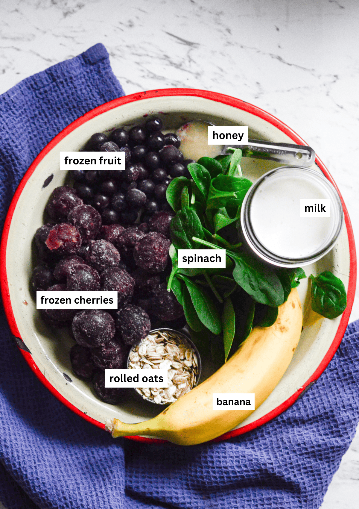 A plate with blueberries, frozen cherries, spinach, honey, milk, banana, rolled oats, ready to go in the blender.