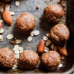 Brown dough balls on a baking sheet with oats and almonds on the pan.