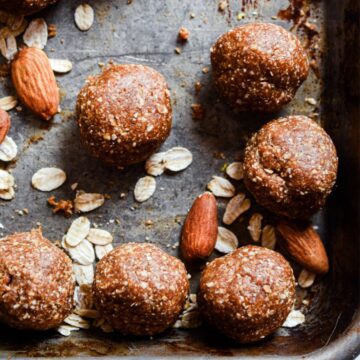 Brown dough balls on a baking sheet with oats and almonds on the pan.
