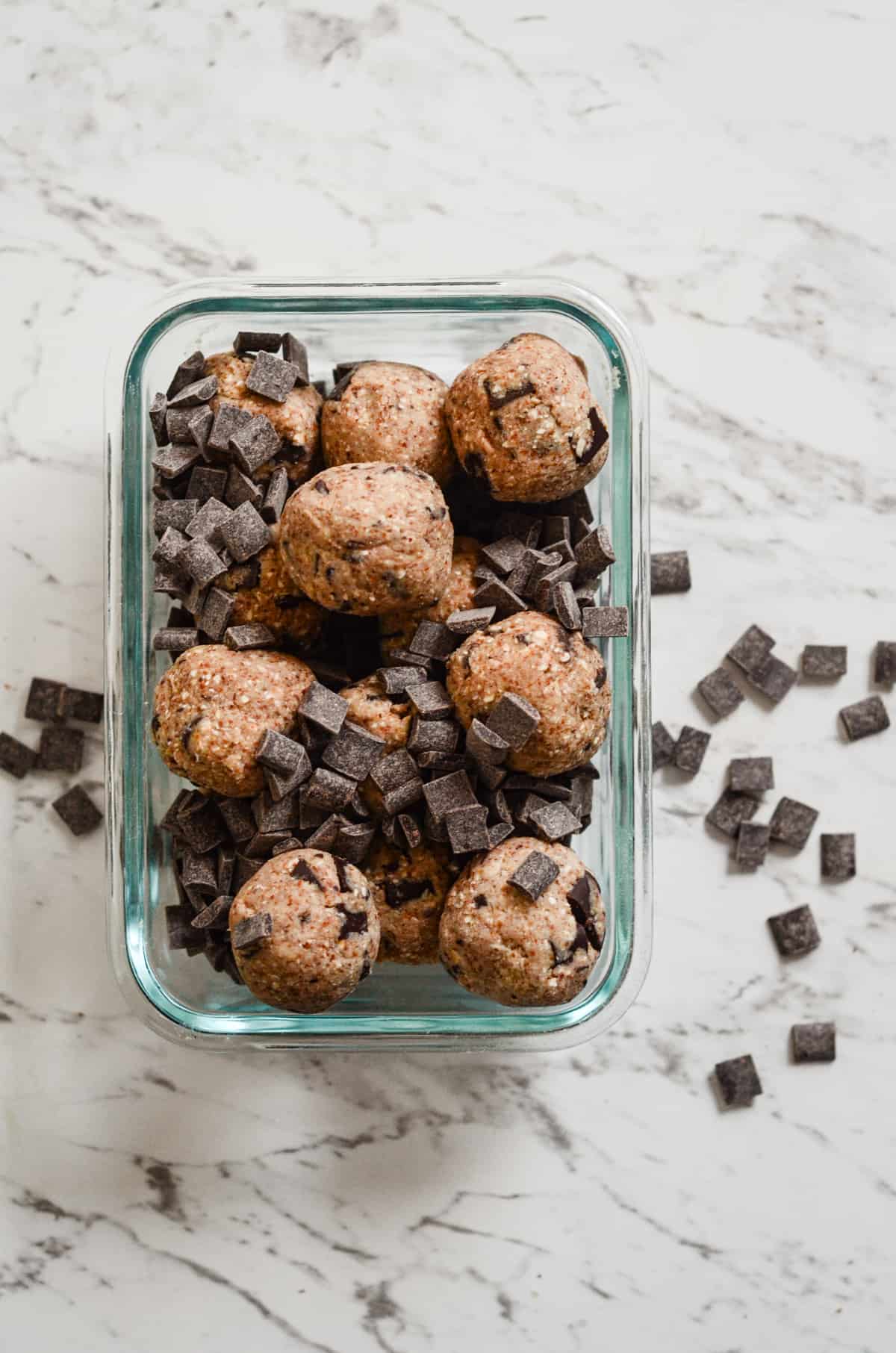 Brown energy balls with chocolate flakes in a glass square container.
