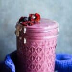 Purple smoothie in a glass jar with frozen sweet cherries and frozen blueberries on top.