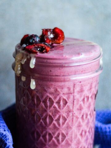 Purple smoothie in a glass jar with frozen sweet cherries and frozen blueberries on top.