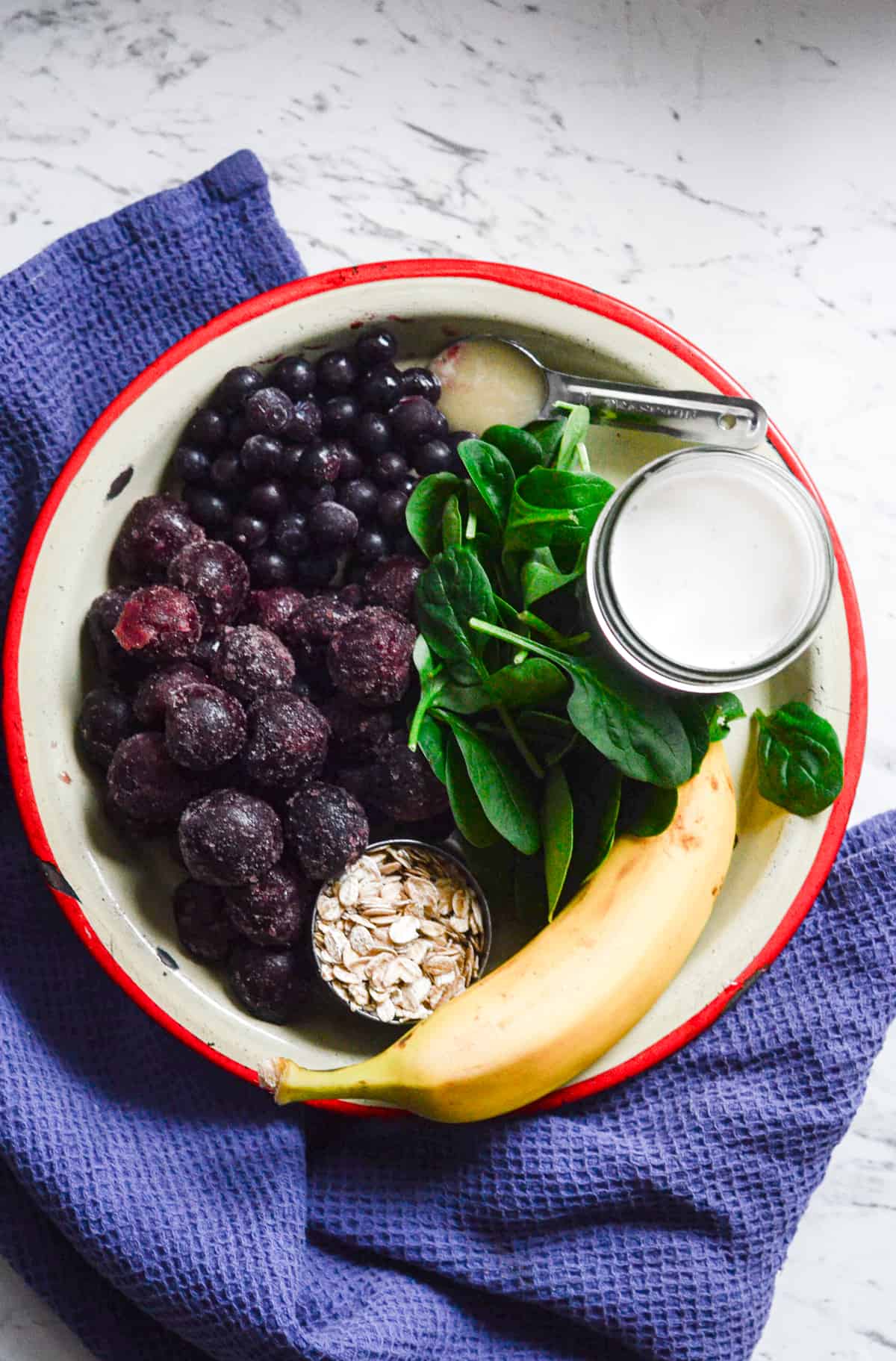 A plate of frozen sweet cherries, frozen blueberries, spinach, almond milk, banana, oats, and honey.