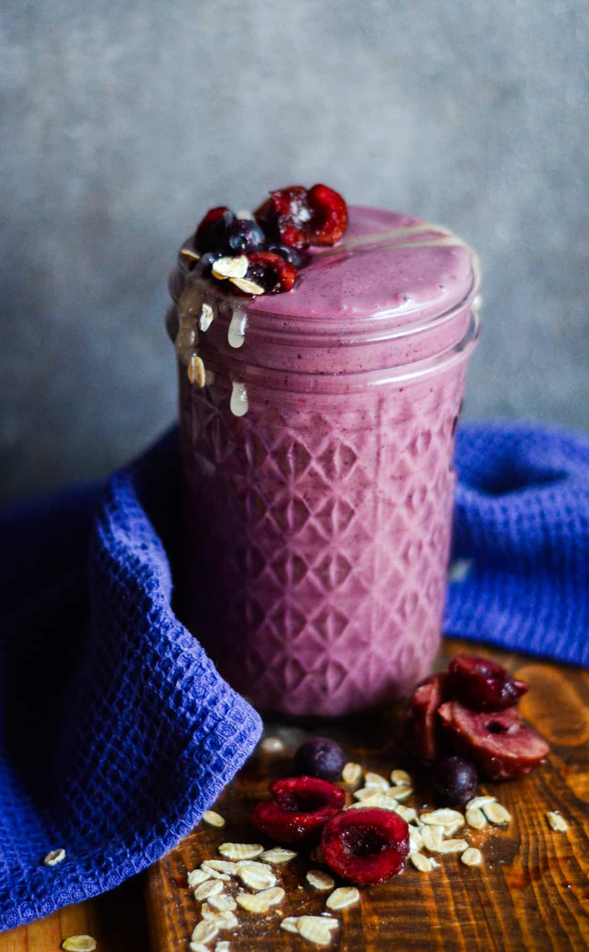 Purple smoothie with cherries in half, blueberries, rolled oats, and honey on top.