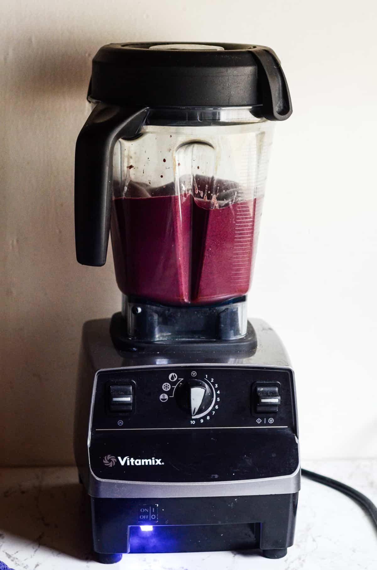 Vitamix with purple smoothie in it being blended.