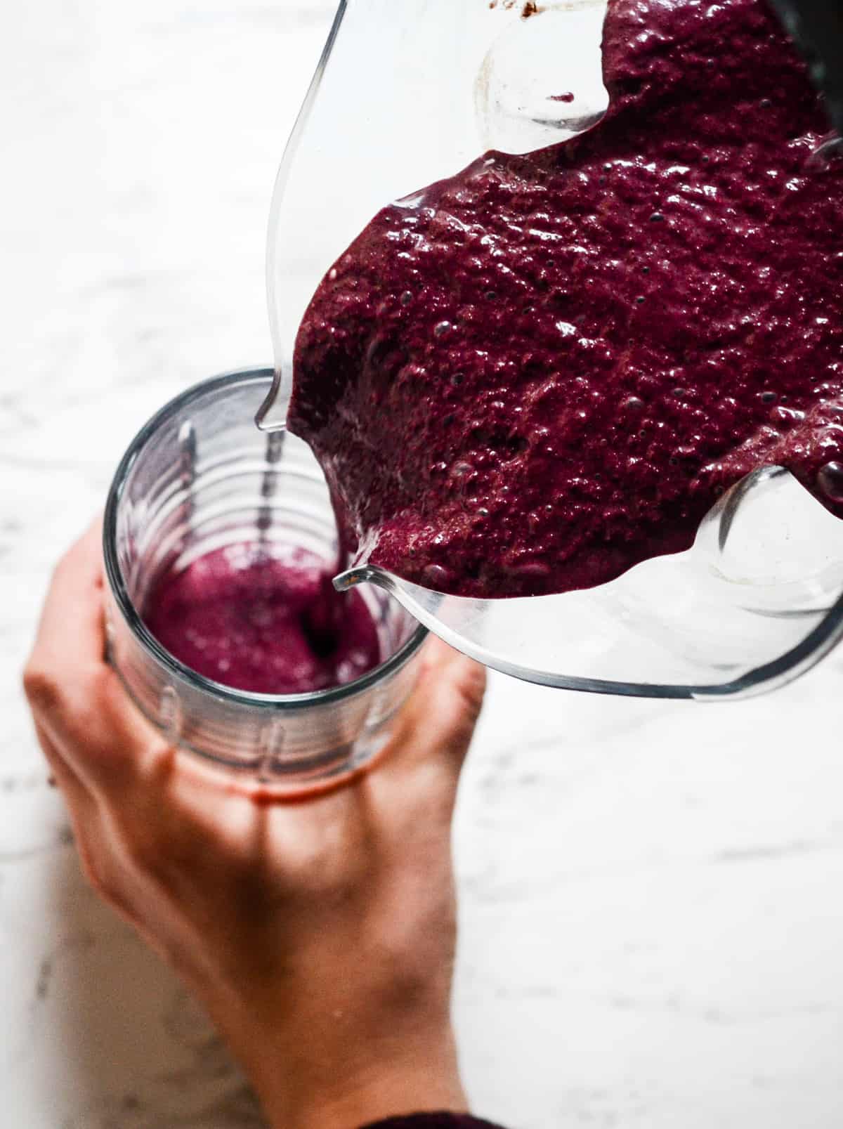 Blueberry smoothie being poured into a glass cup.