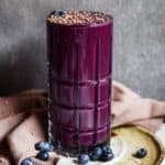 Purple smoothie with chocolate shavings on top, and fresh blueberries on a plate.