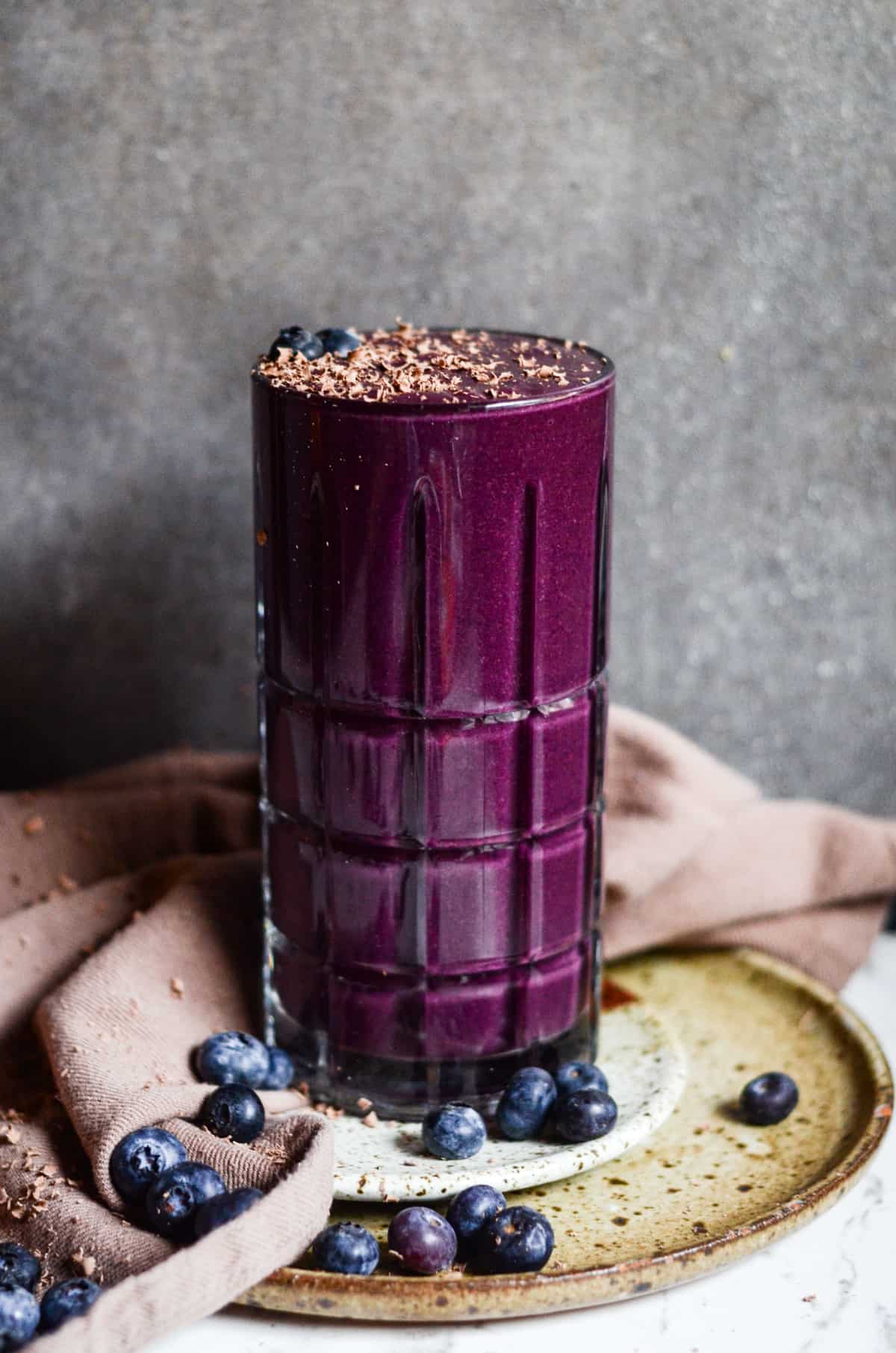Purple blueberry smoothie in a glass cup with fresh blueberries beside it.