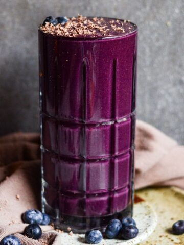 Purple smoothie with chocolate shavings on top, and fresh blueberries on a plate.