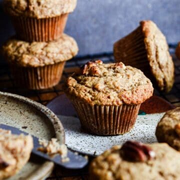 Golden brown muffin with a muffin cup liner with walnuts on top with muffins around it.