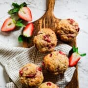 Freshly baked muffins on a wooden platter with strawberries beside it.