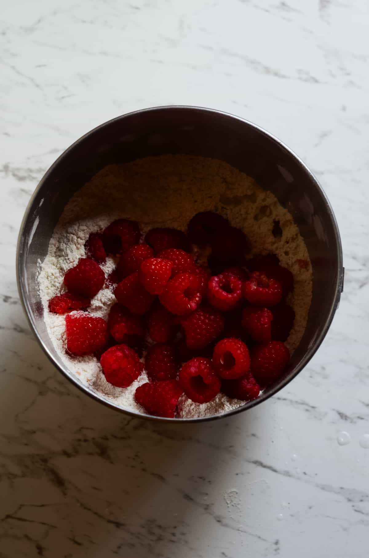 Adding fresh raspberries to a bowl of flour.