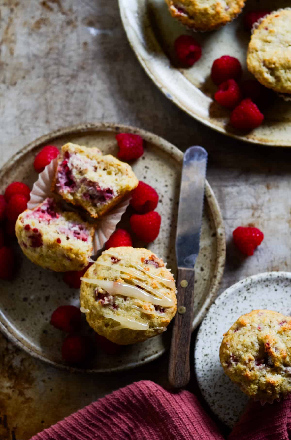 Raspberry muffins on plates with fresh raspberries and a knife.