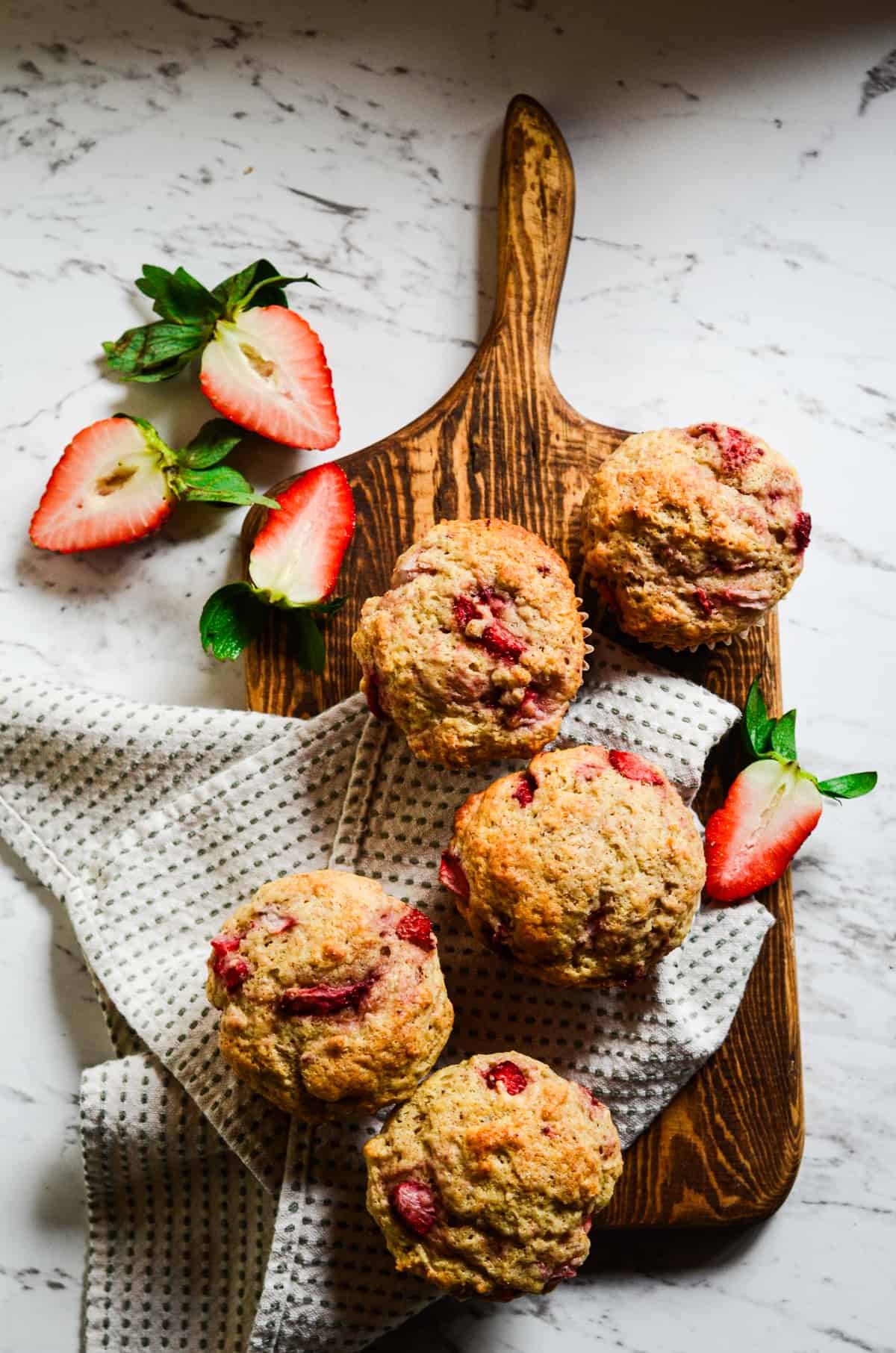 Strawberry muffins on a cutting board with fresh strawberries beside it.