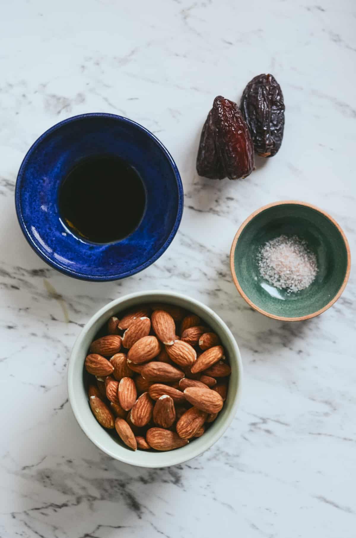 Ingredients needed for homemade almond milk in bowls, vanilla, dates, sea salt and raw almonds.