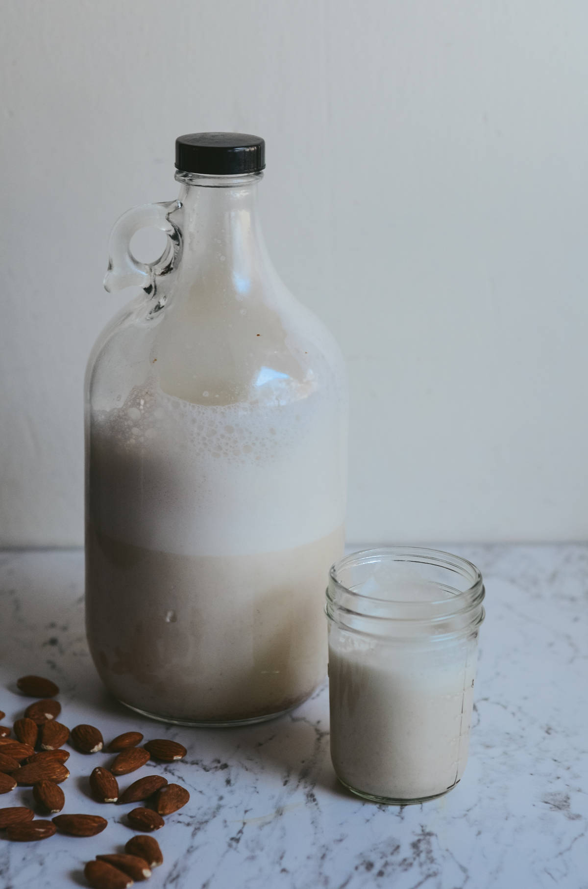 Almond milk in a glass bottle with almonds beside it and a glass of milk beside it.