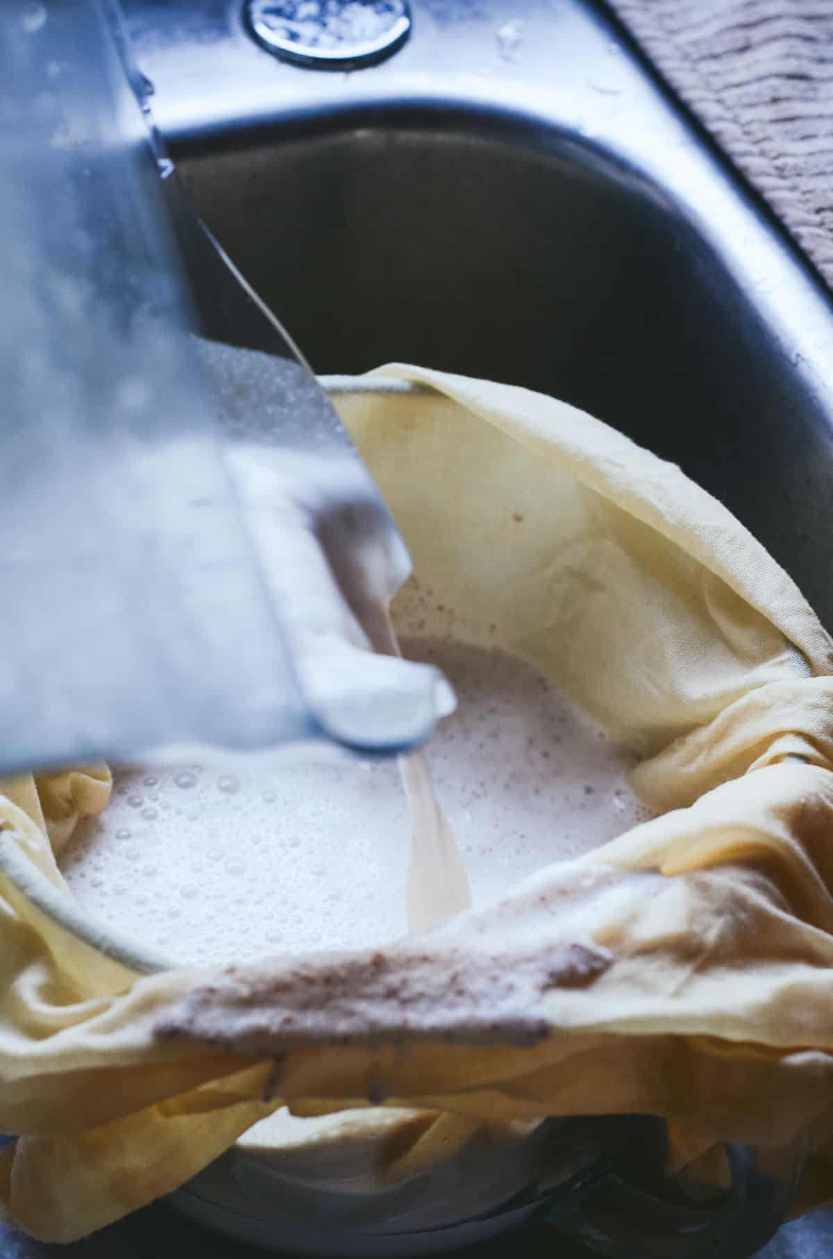 Almond milk being poured into a nut milk bag into a glass bowl.