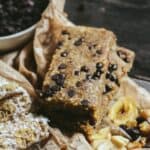 Light brown energy bars with mini chocolate chips on top and yellow banana chips beside it.