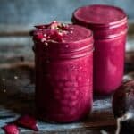 2 glasses of red smoothie with fresh beet beside it.