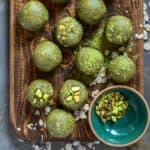 Bright green energy balls on a wood cutting board with matcha and oatmeal beside it.