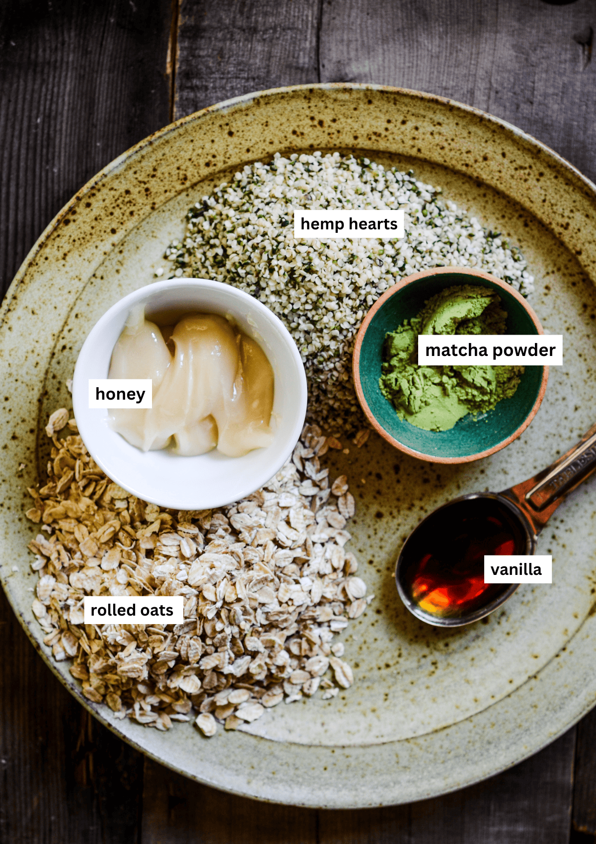 Ingredients for matcha energy balls on a plate, including honey, rolled oats, hemp hearts, matcha, and vanilla.