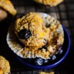 A blueberry peach muffins with the wrapper off the sides of it, and other healthy muffins around it.