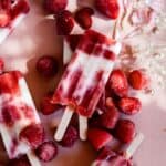 A white and red popsicles with strawberries and rhubarb behind it.