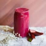 Bright pink smoothie in a glass cup with rhubarb beside it.