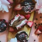 Mini pink cheesecakes on a wooden platter with pink flowers around it.