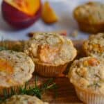 Oat muffins with peach chunks sitting on a wood cutting board with rosemary.