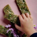 A child's hand reaching for a granola bar with pumpkin seeds on top.