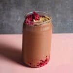 A brownish pink smoothie in a glass with tahini on top with raspberries.