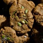 Light brown cookies with pumpkin seeds on top, stacked on more cookies.