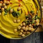 A close up of yellow hummus with chickpeas, pumpkin seeds, paprika, and sea salt.