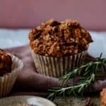 A dark muffin with coarse sugar on top with a little rosemary beside it.