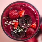 A flat lay photo of a dark red smoothie with hemp hearts, cherries, strawberries, and raspberries on top.