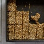 Sliced oat granola bars in a square metal pan on a tile table.