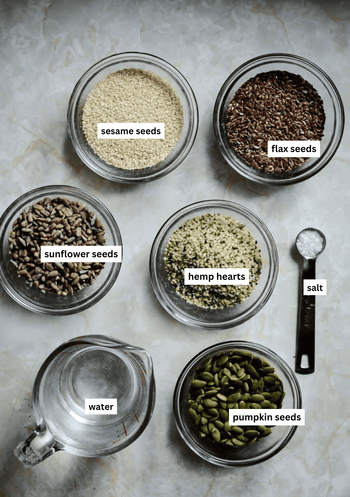 Sesame seeds, flax seeds, hemp hearts, sunflower seeds, sunflower seeds, water, and salt in bowls for crackers.