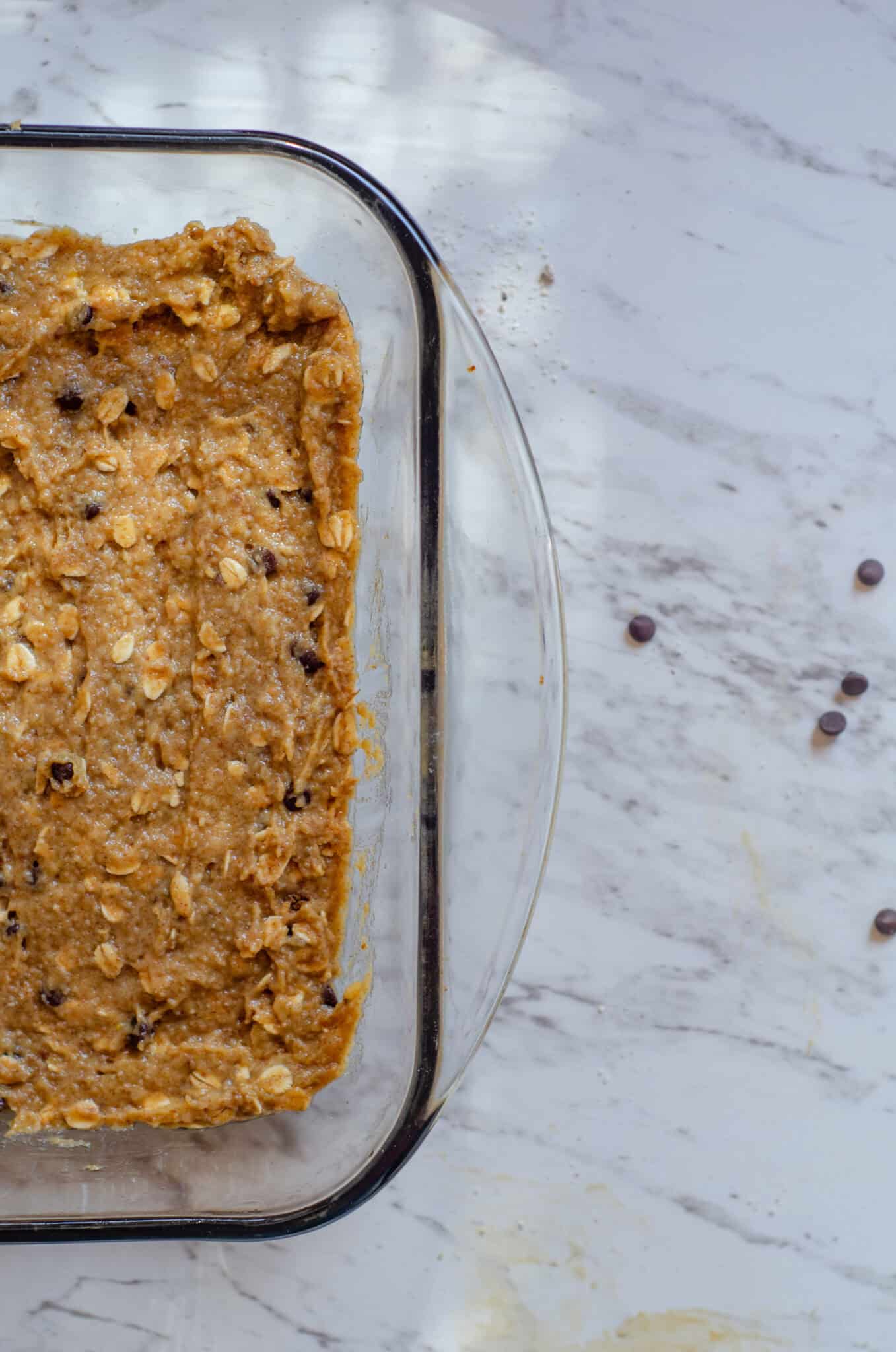 Light brown batter in a 9x13 glass baking pan with flecks of chocolate chips and oats.